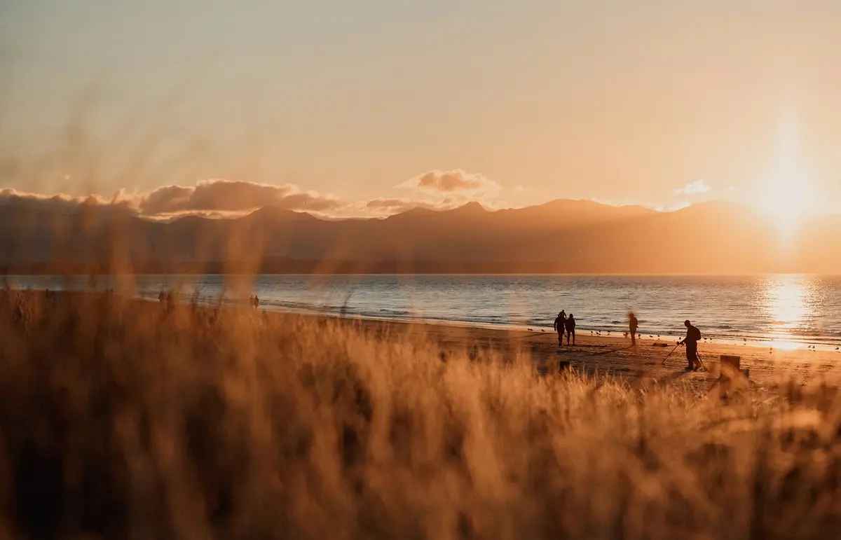 Silhouettes of people coming together on Tahunanui Beach, New Zealand, at sunset